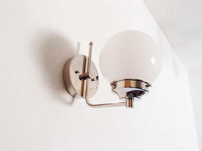 Peut inclure: Une applique murale chrom&eacute;e avec un luminaire blanc en forme de globe. L'applique a un design simple et moderne.