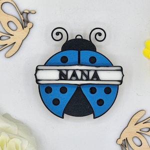 May include: A blue and black wooden ladybug ornament with the word "NANA" written on a white banner. The ladybug has black spots and white accents.