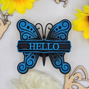 May include: A blue wooden butterfly with intricate details and a black banner that reads "HELLO".
