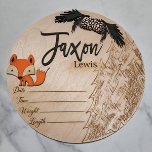 May include: A round wooden plaque featuring a fox illustration, pine tree design, and the name Jaxon Lewis. The plaque has spaces to record the date, time, weight, and length.