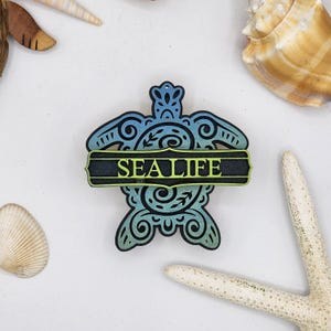 May include: A wooden sea turtle ornament with a blue and green gradient finish. The turtle has intricate details and a banner that reads "SEA LIFE".