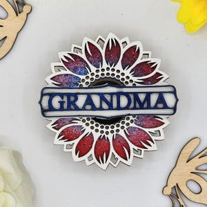 May include: A wooden cutout of a sunflower with red and blue paint, with the word "GRANDMA" in blue lettering on a white banner.