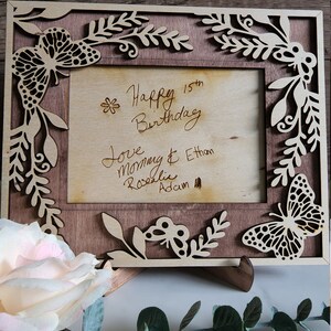 May include: A wooden picture frame with a butterfly design and a handwritten message that reads "Happy 15th Birthday Love Mom & Ethan Rosalie Adam".
