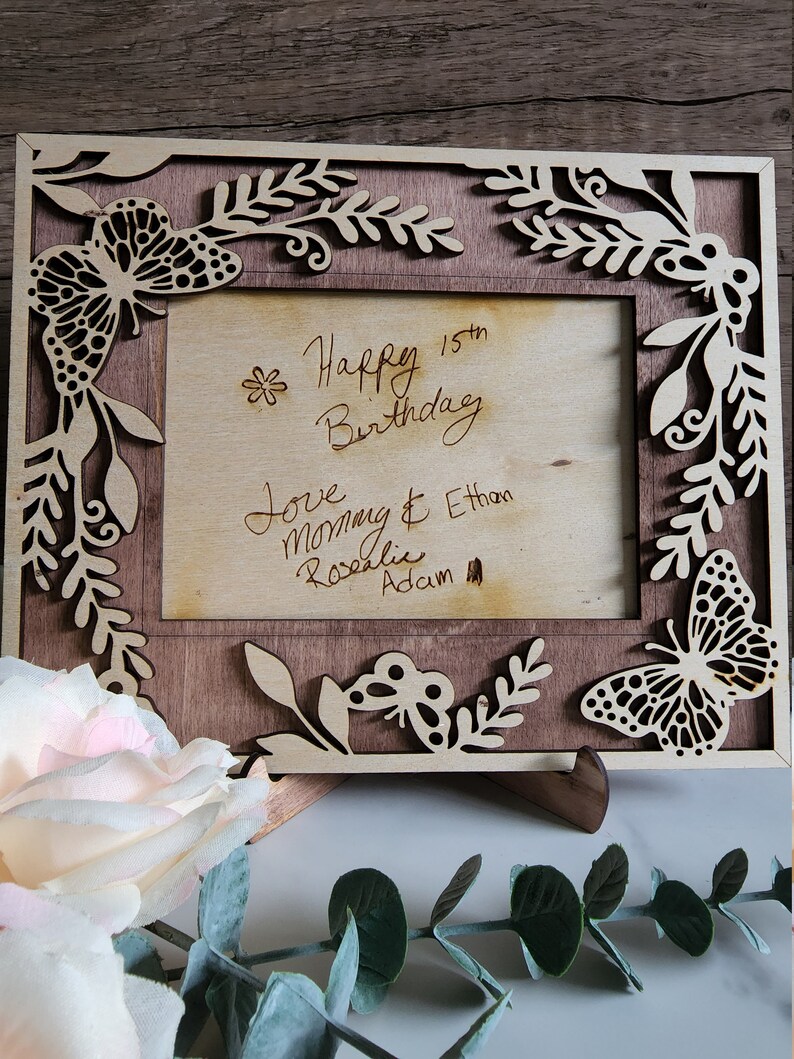 May include: A wooden picture frame with a butterfly design and a handwritten message that reads "Happy 15th Birthday Love Mom & Ethan Rosalie Adam".