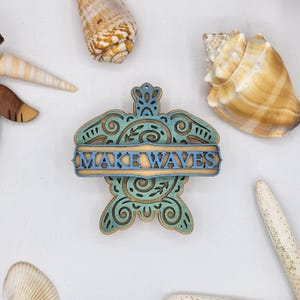 May include: Wooden turtle ornament with a blue and green gradient paint finish. The turtle has a decorative design and a banner that reads "MAKE WAVES".