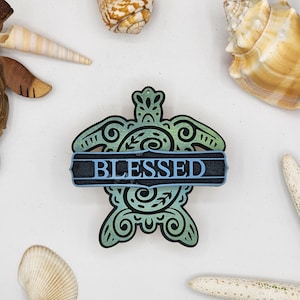 May include: A wooden turtle cutout with a blue and green gradient paint finish. The turtle has intricate details and the word "BLESSED" is written across the centre.