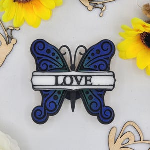 May include: A wooden butterfly with blue and green wings and a white banner with the word "LOVE" in black lettering.
