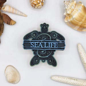 May include: A black and green wooden turtle ornament with intricate details. The turtle has a blue banner across its shell that reads "SEALIFE".