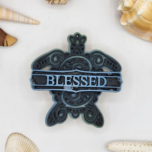 May include: A wooden turtle ornament with a blue and green paint finish. The turtle has a decorative design and the word "BLESSED" is written on a banner across the turtle's shell.