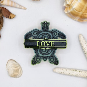 May include: A teal and green wooden turtle ornament with a black banner that reads "LOVE" in yellow lettering.