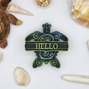 May include: A teal and green wooden turtle with intricate designs and the word "HELLO" on a black banner. The turtle is a decorative wall hanging.