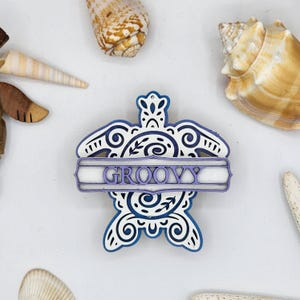 May include: A white wooden turtle ornament with blue and purple accents. The turtle has a decorative design and the word "GROOVY" written on a banner across its shell.