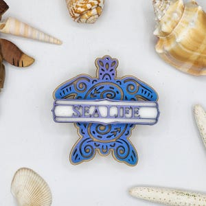 May include: A wooden sea turtle ornament with a blue and purple gradient paint finish. The turtle has intricate details and a banner that reads "SEA LIFE".
