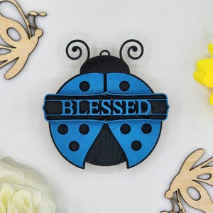 May include: A blue and black wooden ladybug ornament with the word "BLESSED" written across the middle.