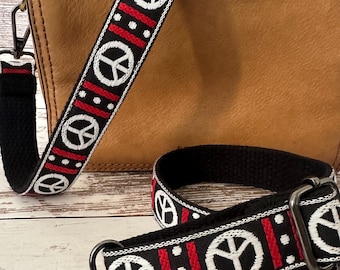 May include: A tan leather handbag with a detachable woven shoulder strap. The strap features a repeating pattern of white peace signs on a black background, accented by vertical red stripes and white dots, with dark metal swivel lobster clasps.