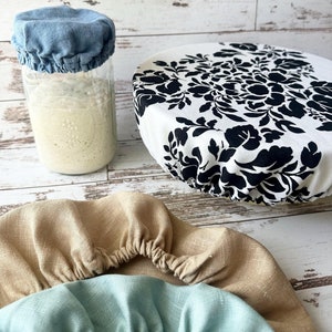 Op de afbeelding: Drie verschillende soorten herbruikbare stoffen hoezen voor voedselopslag. De hoezen zijn gemaakt van natuurlijke materialen en zijn ontworpen om ademend en wasbaar te zijn. De hoezen zijn in verschillende kleuren en patronen verkrijgbaar, waaronder blauw, beige en zwart-wit.