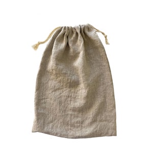 May include: A rectangular drawstring pouch made of light beige, textured fabric. The bag features a gathered top closure secured by two thin, matching beige cords that extend from the sides, with frayed ends visible at the knot points.