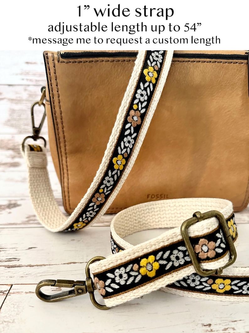May include: A 1 inch wide bag strap with an adjustable length up to 54 inches. The strap features a black center band with embroidered yellow and light brown flowers and white leaves, bordered by cream-colored fabric and antique brass hardware.