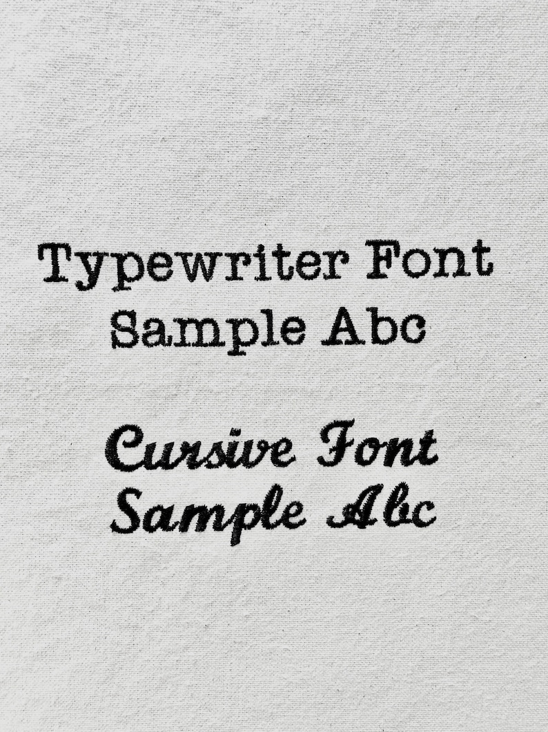 Op de afbeelding: Een close-up van een wit stofoppervlak met twee regels tekst. De bovenste regel luidt "Typewriter Font Sample Abc" in een typemachinelettertype. De onderste regel luidt "Cursive Font Sample Abc" in een cursief lettertype.