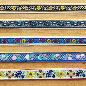 May include: Seven horizontal strips of decorative woven ribbon featuring various patterns including purple floral, black with yellow flowers, blue paisley, blue with red and yellow flowers, blue with cherries, white with floral hearts, and red with flowers.