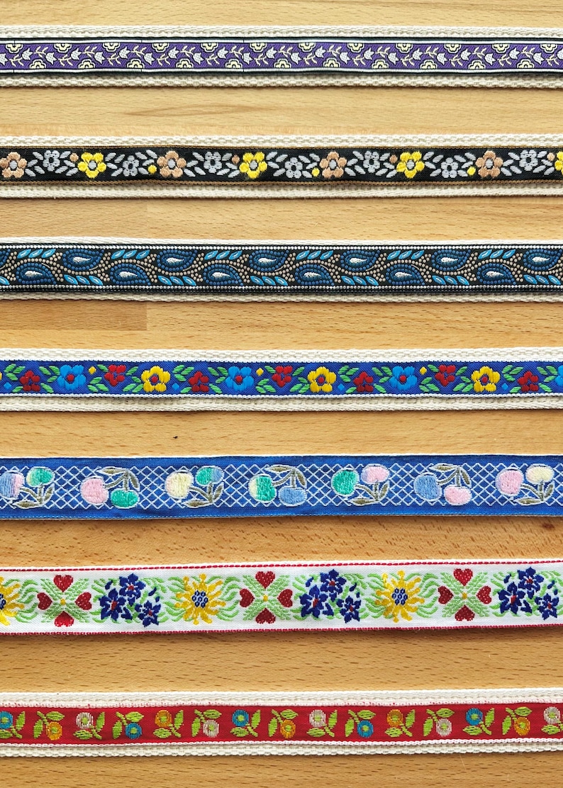 May include: Seven horizontal strips of decorative woven ribbon featuring various patterns including purple floral, black with yellow flowers, blue paisley, blue with red and yellow flowers, blue with cherries, white with floral hearts, and red with flowers.