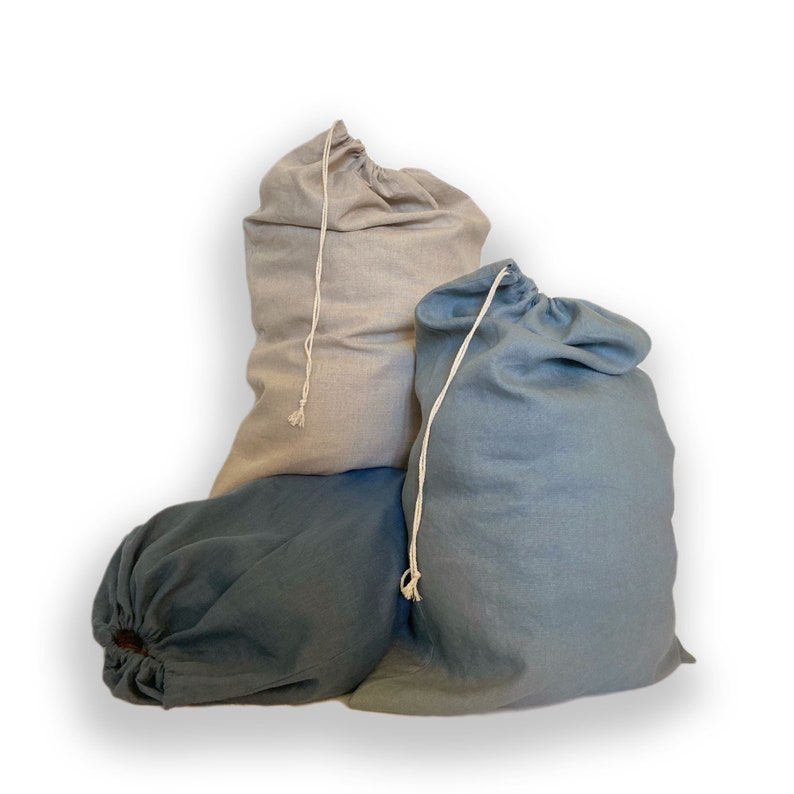 May include: Three fabric drawstring bags in varying shades of blue and light gray. Each bag features a simple woven cord closure at the top, allowing the opening to be cinched shut. The bags have a soft, textured appearance and are arranged together.