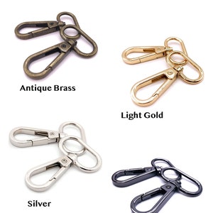 May include: A collection of metal swivel lobster clasps displayed in four distinct finishes labeled Hardware Color: Antique Brass, Light Gold, Silver, and Gunmetal. Each set consists of two connected clasps with a spring-loaded gate mechanism.