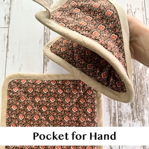 May include: Two brown and red floral print pot holders with a beige trim and a loop for hanging. One pot holder is square, and the other is triangular. The text "Pocket for Hand" is visible on the image.