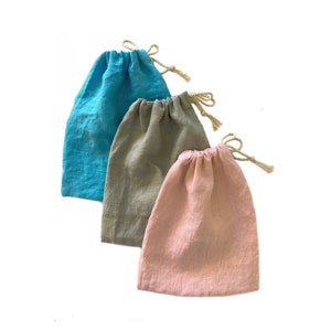 May include: Three drawstring pouches made of a textured fabric, each featuring a different color: one bright turquoise, one muted olive green, and one soft pastel pink. Each bag is cinched at the top with a natural-colored twisted rope cord.