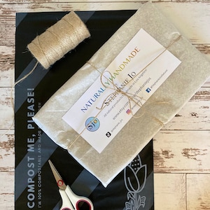 May include: An overhead shot of eco-friendly packaging. A wrapped package is tied with twine, resting on a black and gray compostable mailer. A spool of twine and scissors are also visible. Text reads "Plant Based, Plastic Free Packaging!" and "COMPOST ME, PLEASE!"