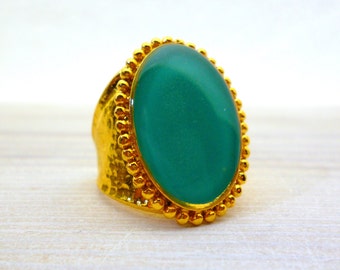 May include: A gold ring with a large oval green stone set in a beaded bezel.