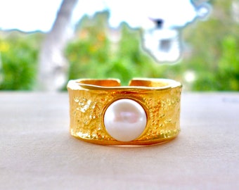 May include: A gold ring with a textured band and a white pearl in the centre.