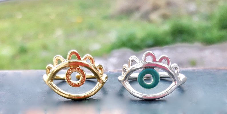 May include: Two eye rings, one gold and one silver, with a detailed eye design. The gold ring has a plain eye, while the silver ring has a green eye.