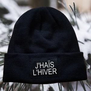 May include: Black beanie with a white patch that says "J'HAIS L'HIVER" on a snowy background.
