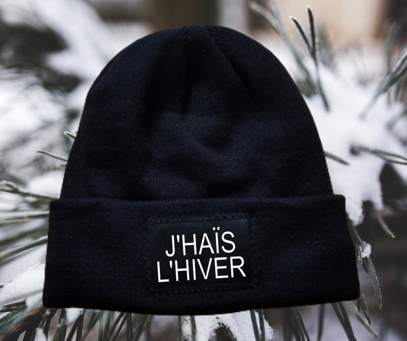 May include: Black beanie with a white patch that says "J'HAIS L'HIVER" on a snowy background.