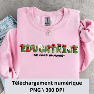 Könnte beinhalten: Ein hellrosa Sweatshirt mit dem Wort "EDUCATRICE" in grünen Buchstaben, verziert mit Marienkäfern und Gänseblümchen. Darunter steht der Text "-DE MINIS HUMAINS-". Eine silberne Halskette befindet sich auf dem Sweatshirt.