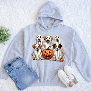 May include: A pale grey hoodie with a Halloween design. The graphic shows five dogs in ghost costumes, a carved pumpkin, and a smaller pumpkin. The hoodie is shown with blue jeans and white trainers.