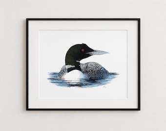 May include: A framed art print featuring a detailed illustration of a common loon floating on water. The bird has a black head, a red eye, a white neck patch with black stripes, and a black back with white spots, set in a thin black frame.