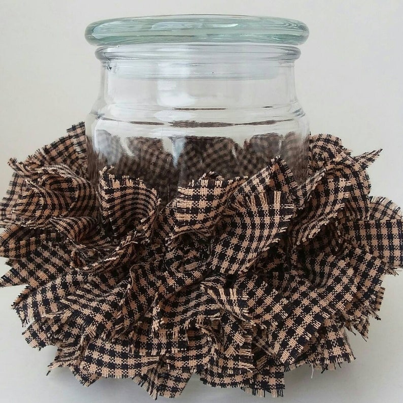 May include: A clear glass jar with a lid, decorated with a brown and black checkered fabric ruffle.