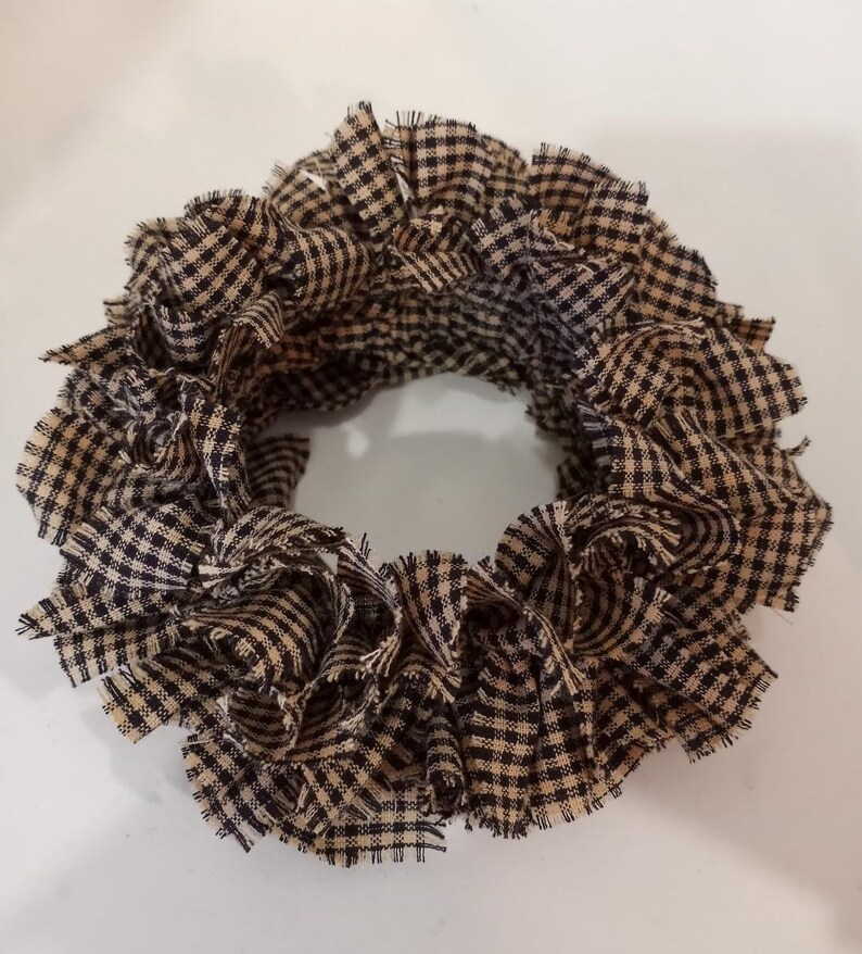 May include: A brown and black gingham fabric wreath. The fabric is frayed and gathered to create a full, round shape.