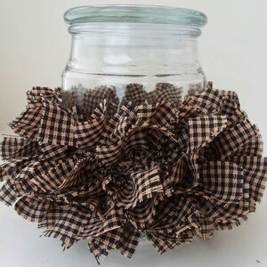 May include: A clear glass jar with a black and tan checkered fabric ruffle around the bottom.