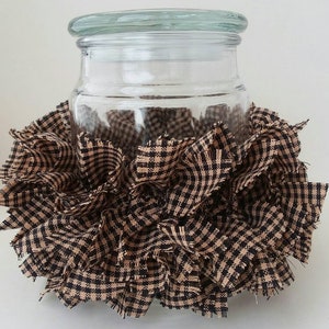 May include: A clear glass jar with a lid is surrounded by a brown and black gingham fabric. The fabric is ruffled and gathered around the jar.