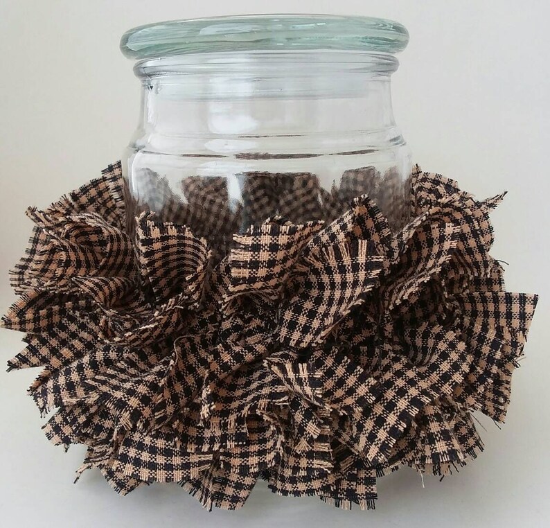 May include: A clear glass jar with a lid is surrounded by a brown and black gingham fabric. The fabric is ruffled and gathered around the jar.