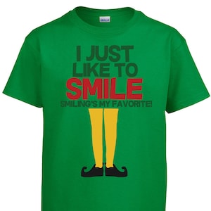 May include: Green t-shirt with the text "I just like to smile" in black and red. The text "Smiling's my favourite!" is in black below the main text. A cartoon elf's legs and shoes are below the text.