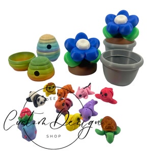 Op de afbeelding: Een verzameling kleurrijke, miniatuur 3D-geprinte beeldjes en decoratieve items. De collectie omvat een blauwe bloem in een pot, bijenkorven en diverse dierenfiguren zoals een panda, leeuw en schildpad. De tekst "Custom Design Shop" is ook zichtbaar.