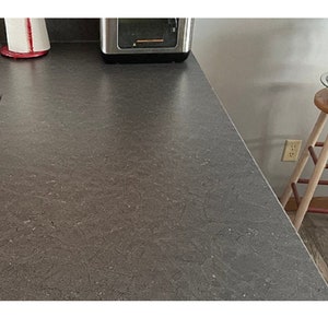 K&ouml;nnte beinhalten: Nahaufnahme einer grauen Arbeitsplatte mit einem gesprenkelten Muster. Die Arbeitsplatte ist glatt und scheint aus einem strapazierf&auml;higen Material zu bestehen.