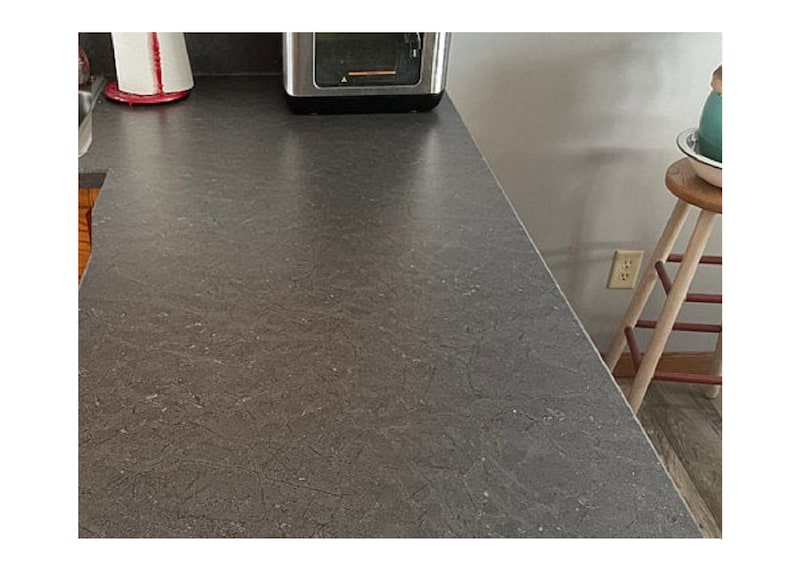 K&ouml;nnte beinhalten: Nahaufnahme einer grauen Arbeitsplatte mit einem gesprenkelten Muster. Die Arbeitsplatte ist glatt und scheint aus einem strapazierf&auml;higen Material zu bestehen.