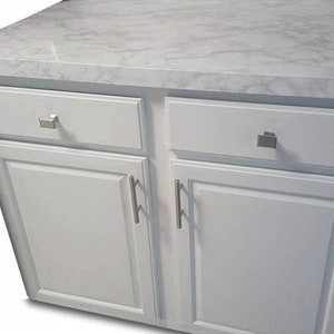 May include: White kitchen cabinet with two drawers and two doors. The cabinet has silver hardware and a white marble countertop.