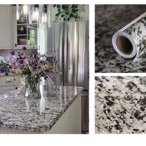May include: Close-up of a white and black granite countertop with a vase of purple flowers on top. The countertop is made of a self-adhesive contact paper that looks like real granite.