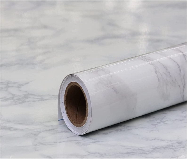 May include: A roll of white marble contact paper with a gray veining pattern. The paper is rolled up and the end of the roll is visible.